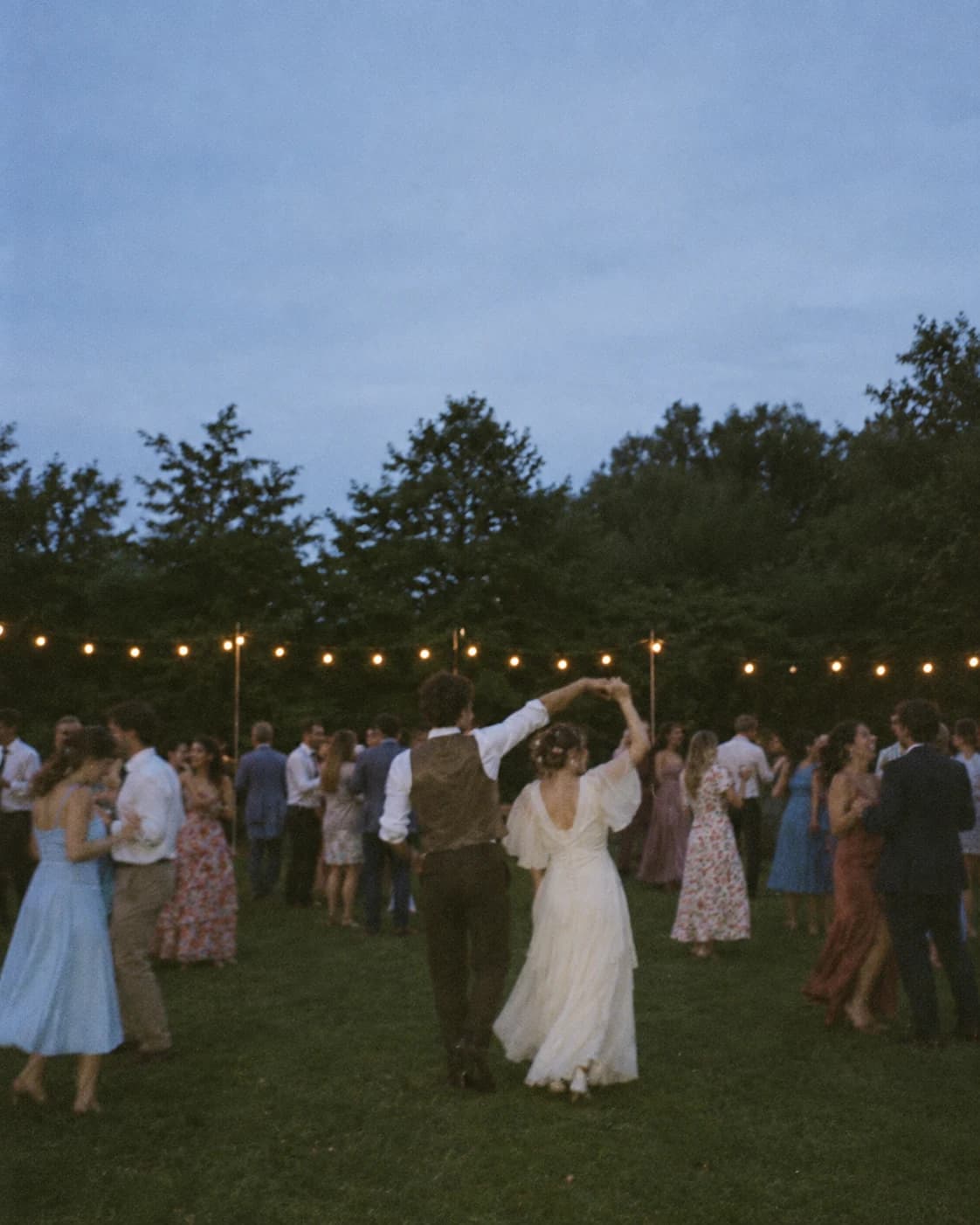 Wedding guests dancing under string lights in a garden at dusk